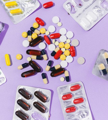 Close-up of various pills and capsules on a purple backdrop, showcasing pharmaceutical diversity.